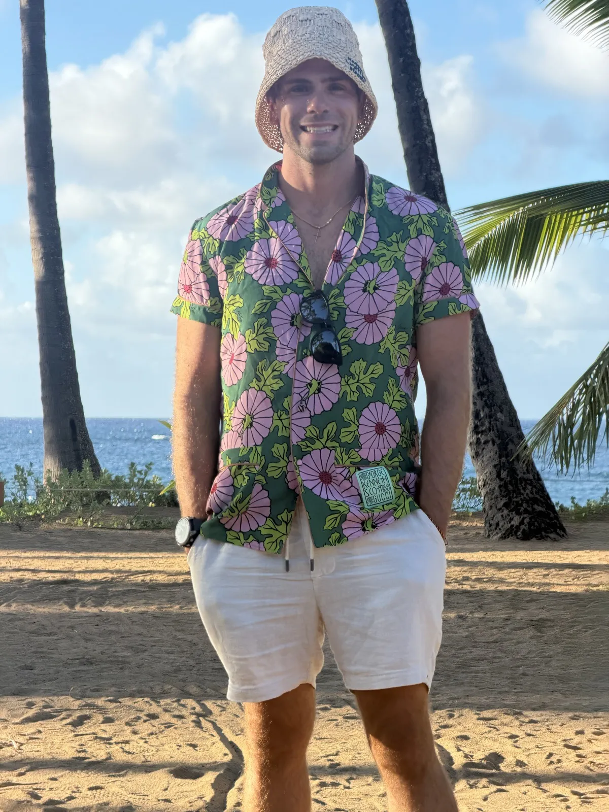 Nick in a bucket hat and pink floral shirt on a beach